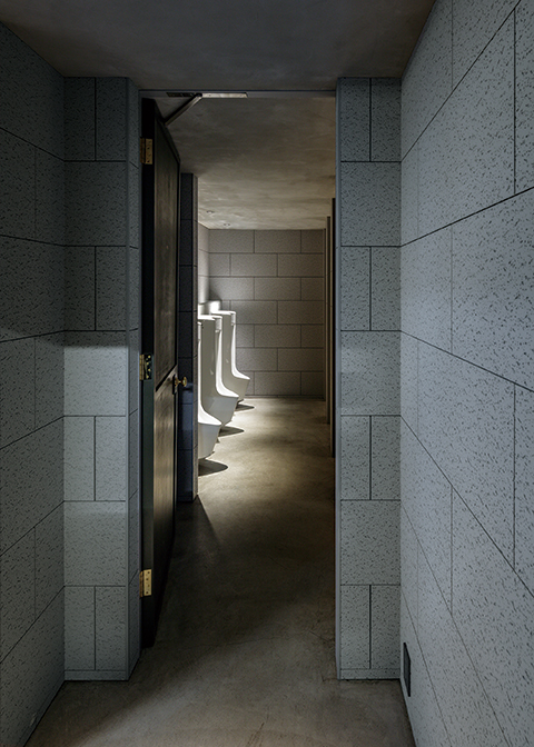 研究開発棟1階男子トイレを前室から見る。INAXの自動洗浄センサー付き小便器。照度や素材のカラートーンを抑え、落ち着いた上質な空間としている