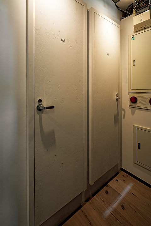 トイレ個室前の通路。壁面から突き出るように扉と枠部分を設け、個室内部の奥行きを最大限確保している