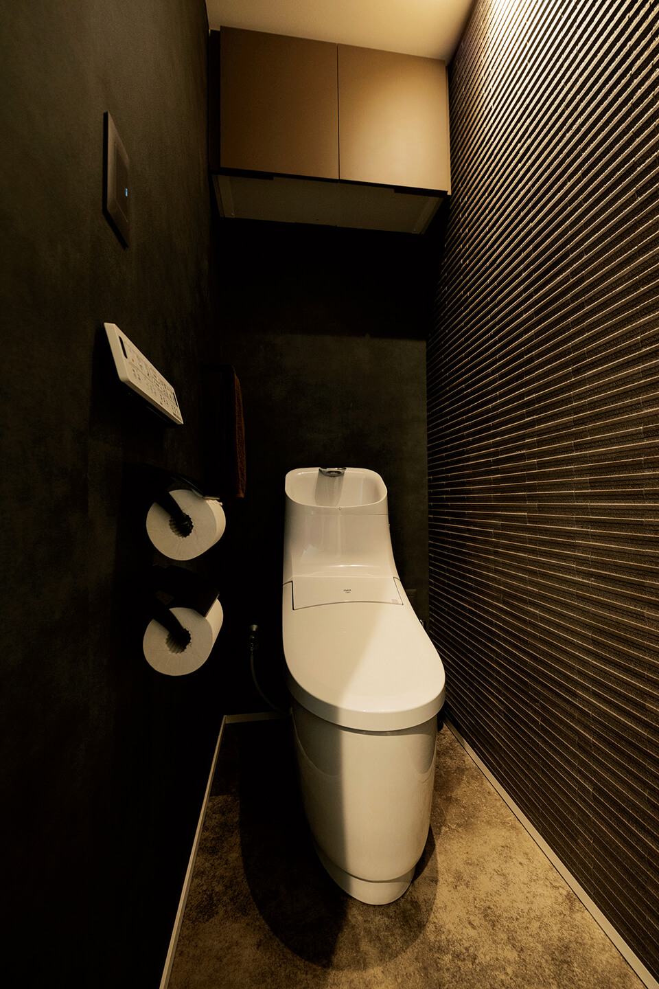 トイレはリラックスできるようダークトーンで仕上げ、あえて1灯のユニバーサルダウンライトで壁を照らす照明計画とした