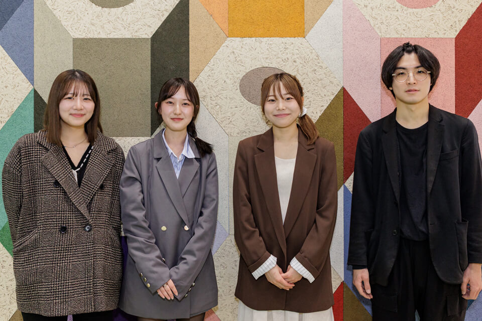 壁面をデザインした日本工学院専門学校の2年生。左から中島さん、松井さん、村上さん、小玉さん。中島さんデザインによる、レノウッドの塗装カラーバリエーションを示した立体感のある壁面の前で撮影