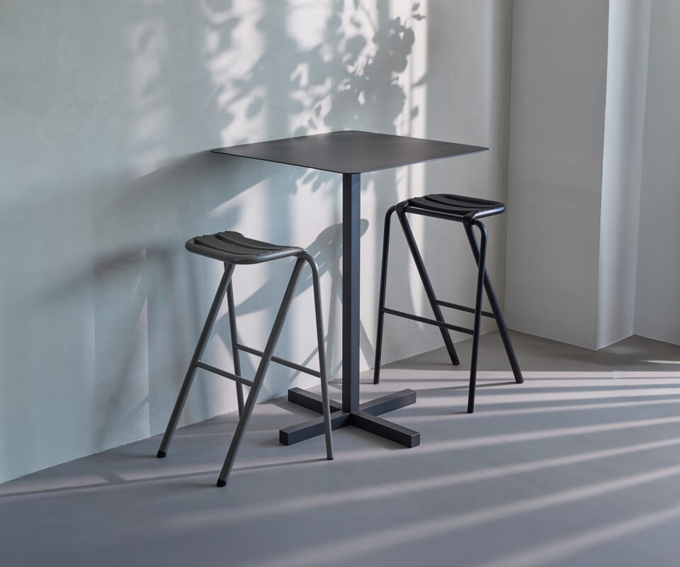 「BENT HIGH STOOL」と「SOLID STEEL HIGH DINER TABLE SQUARE」の組み合わせ。ハイスツールはブラックとシャンパンの2色展開。サイズ：w420×d355×h630（ sh617）㎜、価格：26,400円。ハイテーブルスクエア サイズ：w600×d600×h850㎜、 価格：108,900円。ラウンドトップはφ 700㎜、価格：115,500円