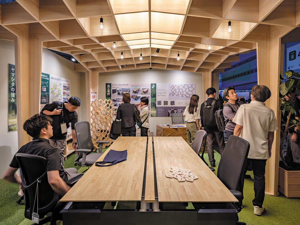木製デスクやパーティション、施工事例パネルを並べたブース内部。初日から多くの来場者が立ち寄り、木製オフィス家具の質感や価格帯への関心の高さがうかがえた